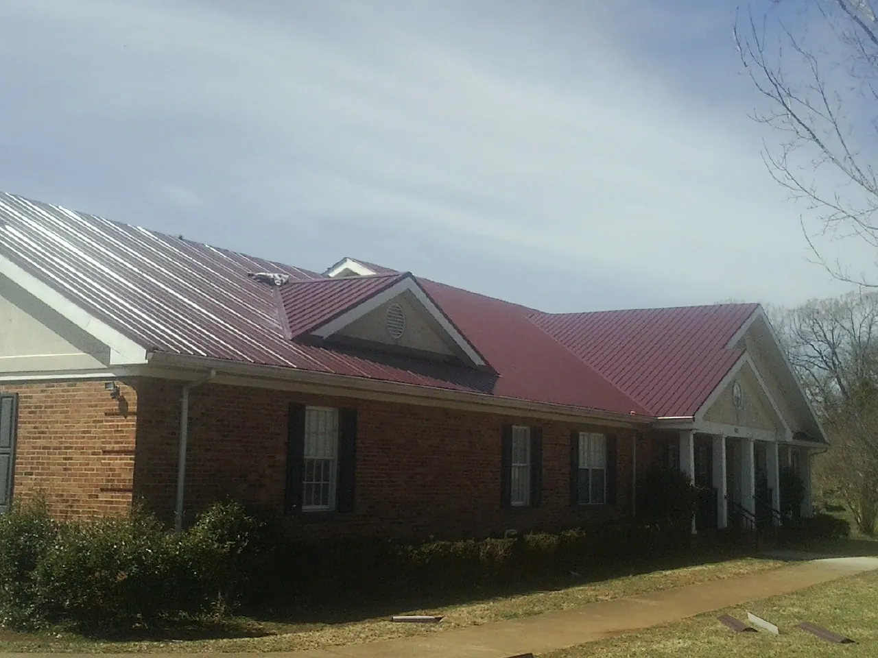 Red metal roof with gabled entries on a long brick building, from a Hail Damage Roof Repair job in Shapleigh