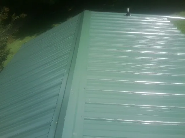 New green metal panels meeting at the ridge of a roof — Flat Roof Repair work by our crew in Shapleigh
