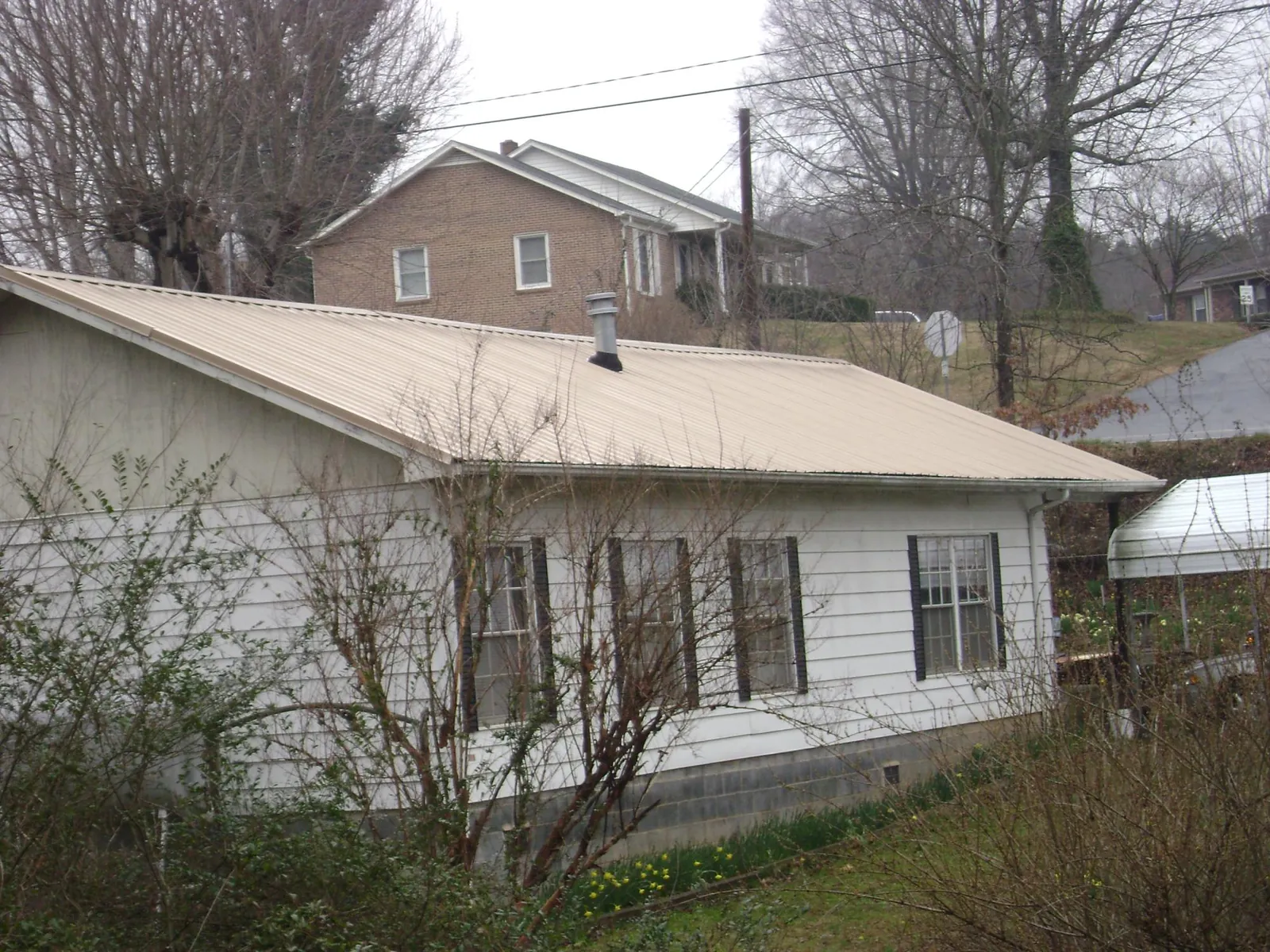 Tan metal roof on a white sided house set into a hillside — Commercial Roofing by Roofing Brothers in Shapleigh