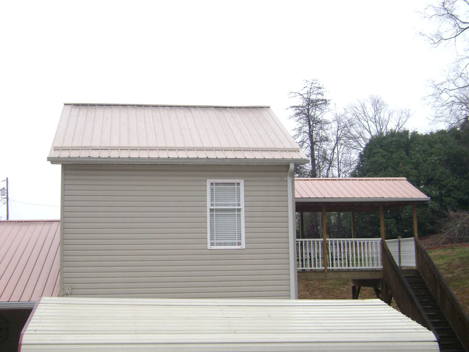Tan metal roofs on a two story addition and attached porch, from a Roof Replacement job in Shapleigh
